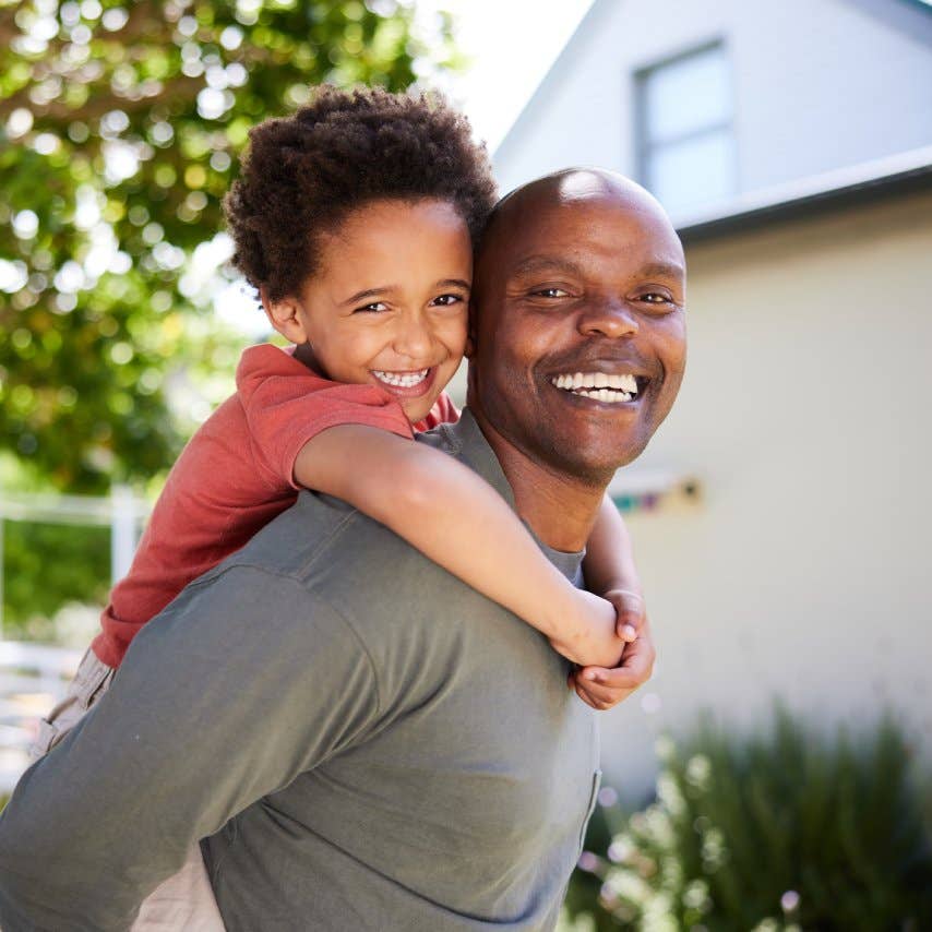 Dad carrying his cute little son on his back outside in summer