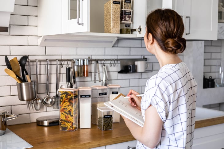 Woman making a grocery list in an organized kitchen